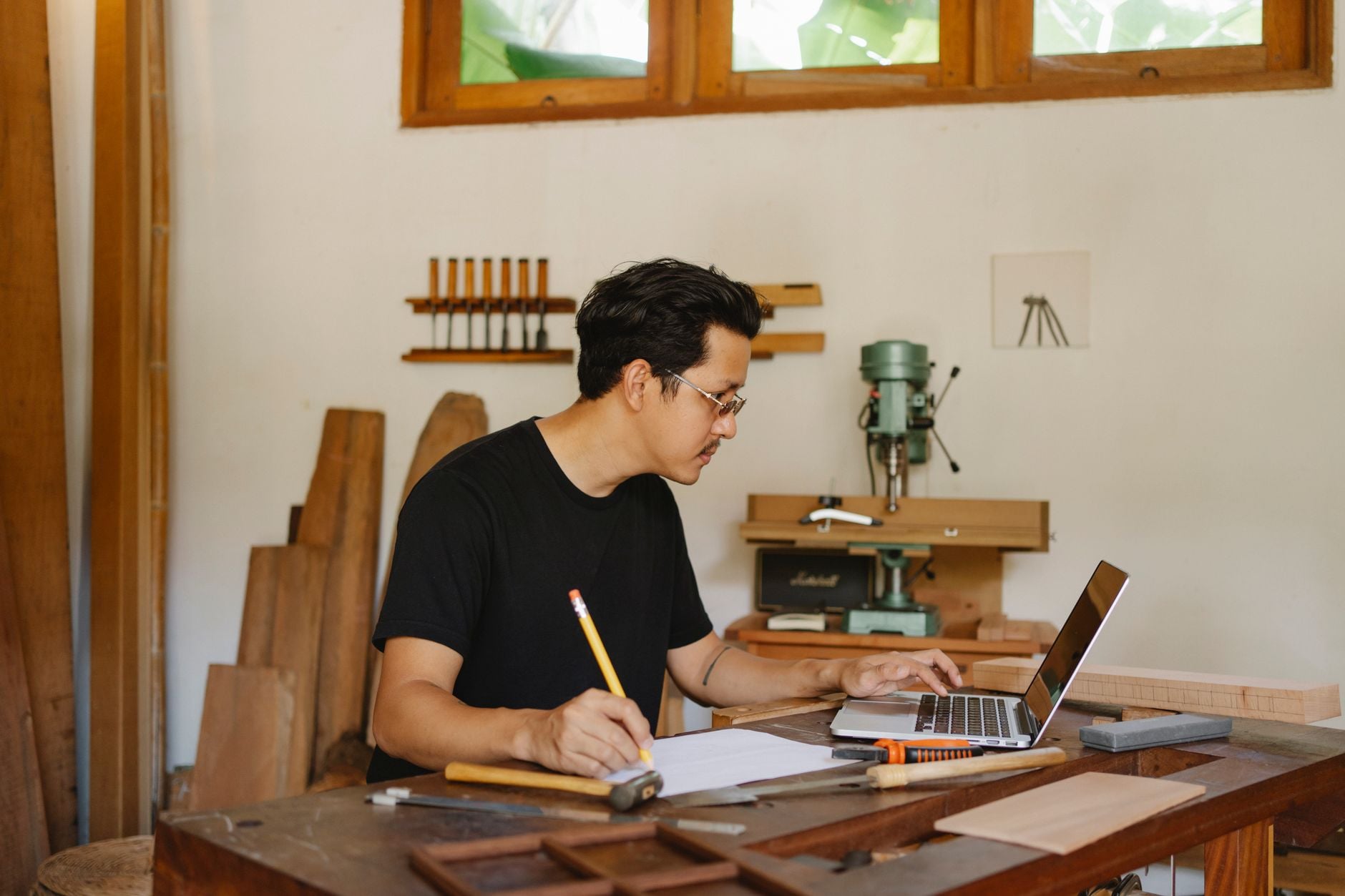 A man working at a wooden desk with a notebook and laptop