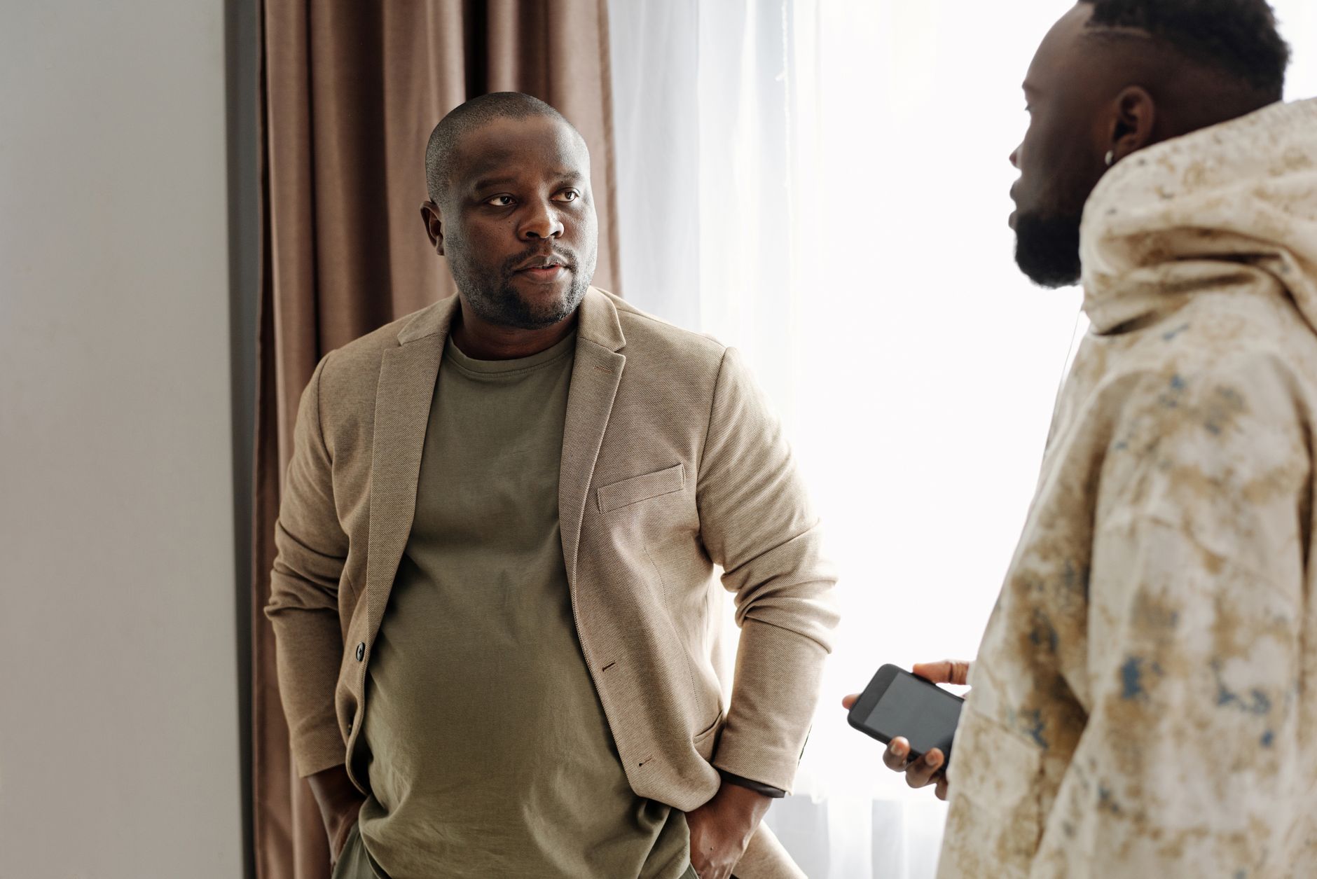 Two men standing together, one looking away